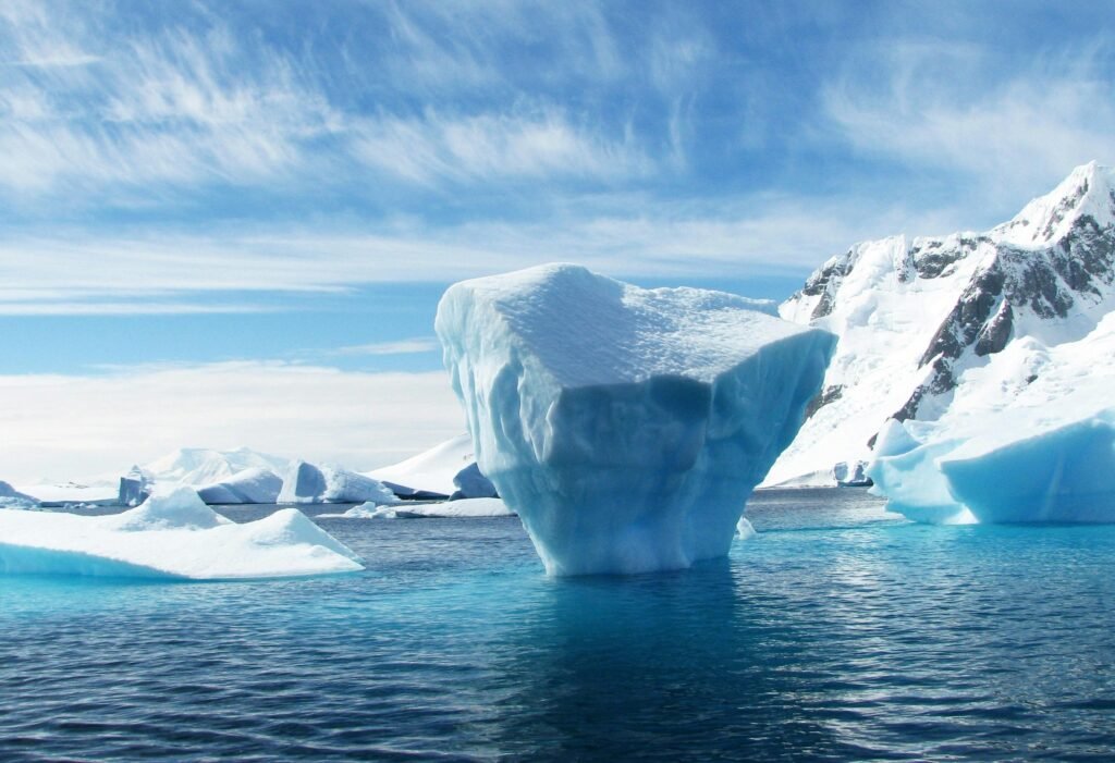 A stunning iceberg floating in the cold, pristine waters with a backdrop of snowy mountains.