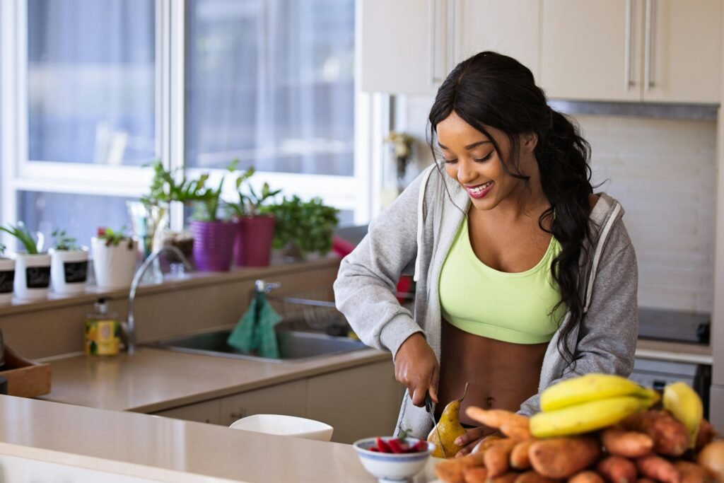 Smiling woman preparing fresh fruit in a sunlit kitchen, embodying a healthy lifestyle.