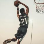 A dynamic basketball player executing a slam dunk during a vibrant outdoor game.