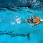 Top view of a swimmer wearing a cap, performing a front crawl stroke in a clear blue swimming pool.