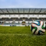 Close-up of a soccer ball on a lush grass field with an empty stadium in the background.